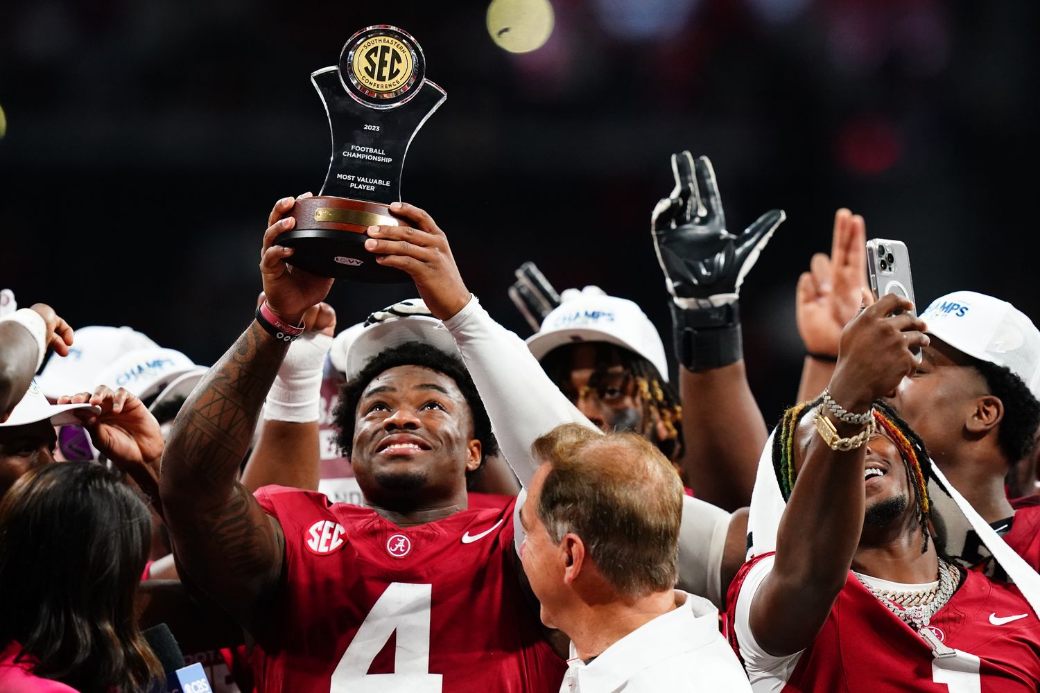 Jalen Milroe raises his SEC Championship MVP trophy above his head as Nick Saban stands next to him